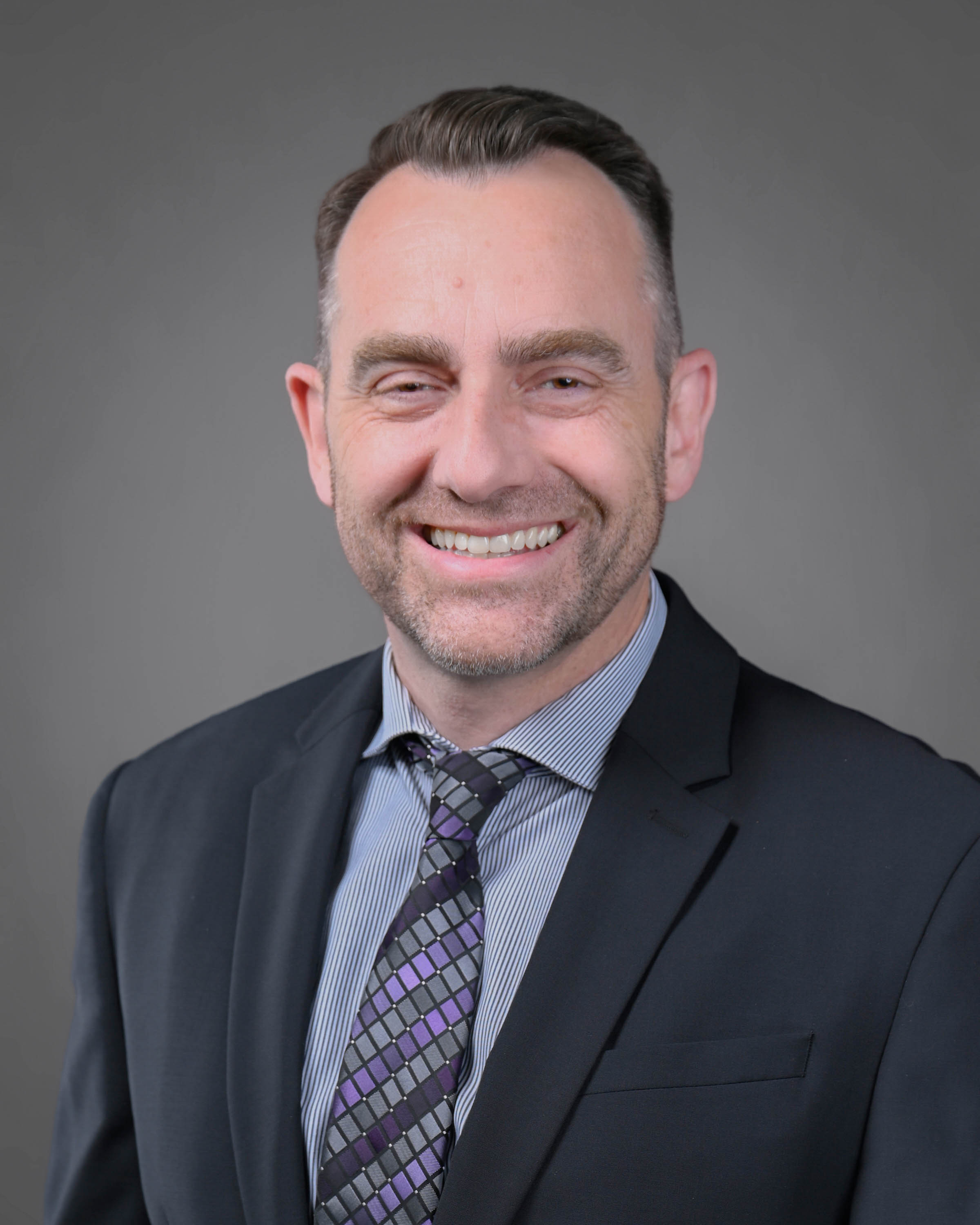 Man with dark hair in dark suit smiling